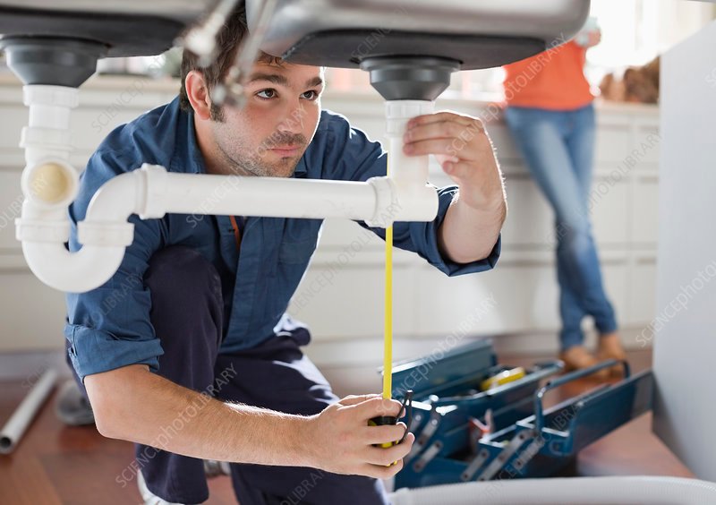 Plumber working on pipes under kitchen sink.